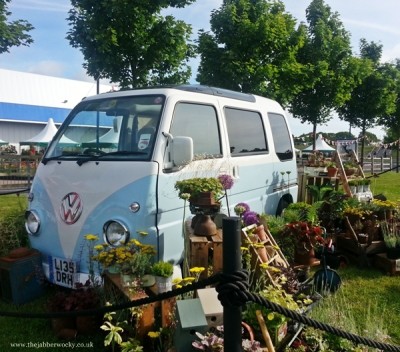 A teeny tiny VW van, surrounded by plants.
