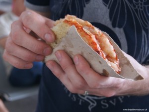 A folded pizza bought from a street vendor and wrapped in card
